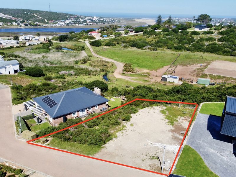 Aerial view of a vacant residential plot outlined in red, situated in a coastal estate with surrounding natural landscape and nearby residential properties.