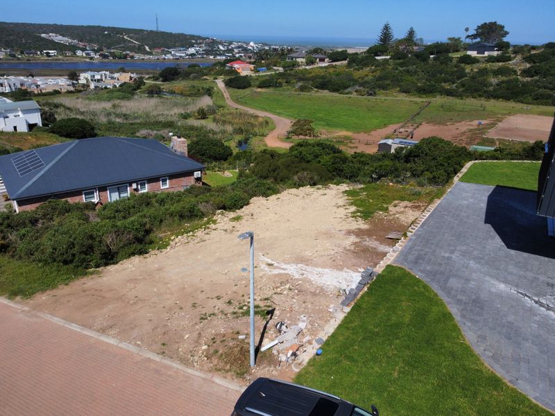 Aerial view of a vacant residential plot featuring a paved driveway, retaining wall, and street light, with surrounding landscape and coastal views.