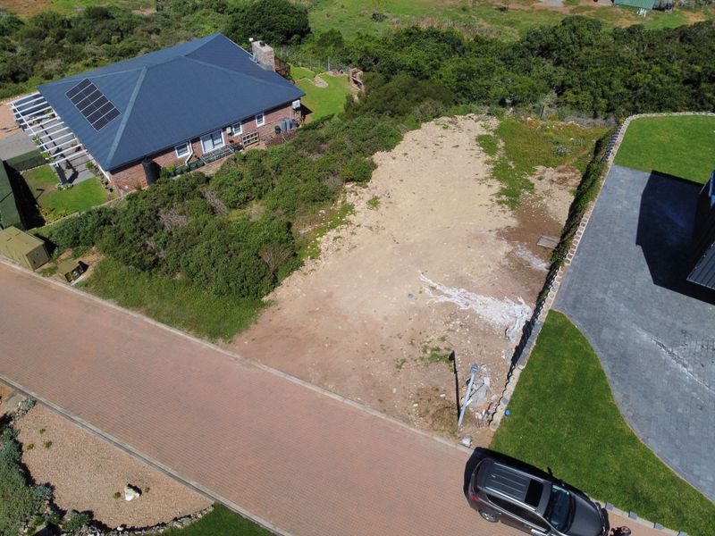 Aerial view of a vacant residential plot situated between existing properties, featuring a paved street frontage and natural vegetation.