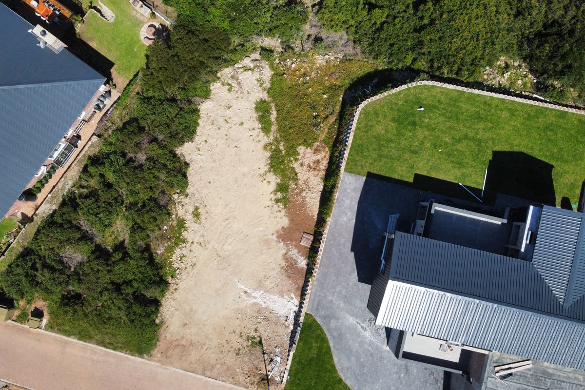 Aerial view of a residential vacant land plot adjacent to an existing home with a paved driveway and established lawn.