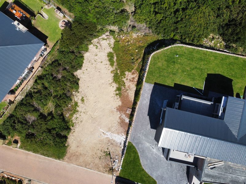 Aerial view of a residential vacant land plot adjacent to an existing home with a paved driveway and established lawn.