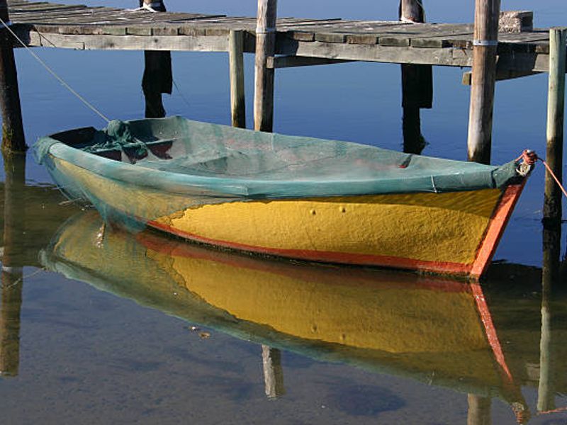A view of a small wooden jetty extending over calm water, featuring a moored boat.