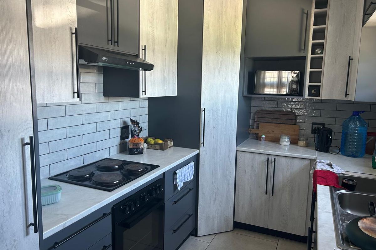 Modern kitchen featuring two-tone cabinetry, subway tile backsplash, integrated electric hob and oven, and ample storage with a built-in microwave shelf.
