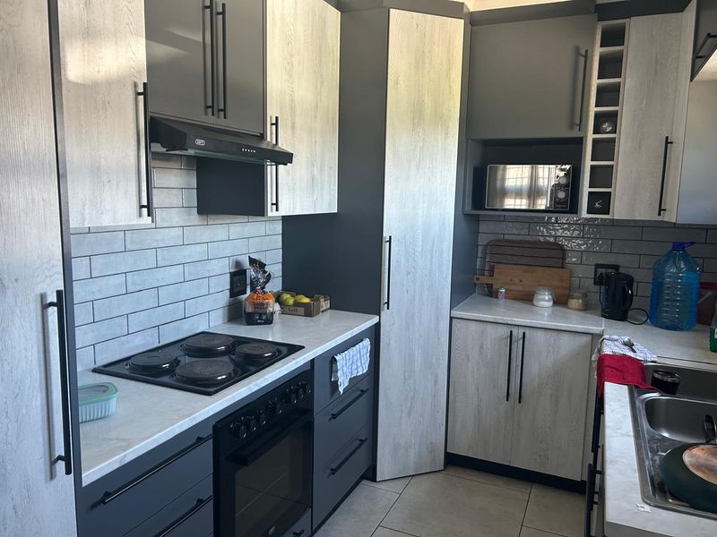 Modern kitchen featuring two-tone cabinetry, subway tile backsplash, integrated electric hob and oven, and ample storage with a built-in microwave shelf.