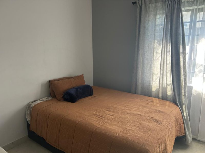 A simple bedroom featuring neutral wall tones and a window with curtains, providing a functional and comfortable sleeping space.