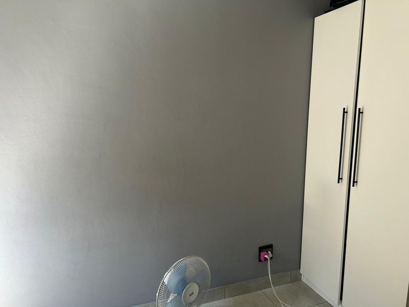 A bedroom interior featuring a built-in white wardrobe with modern handles and tiled flooring.