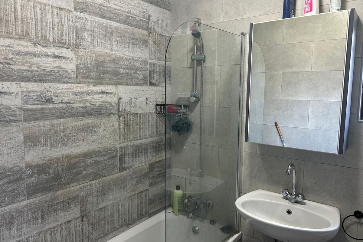 Modern bathroom featuring a bathtub with a glass shower screen, wall-mounted basin, and a mirrored medicine cabinet with contemporary tiled wall finishes.