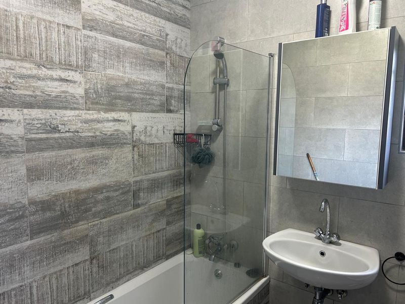 Modern bathroom featuring a bathtub with a glass shower screen, wall-mounted basin, and a mirrored medicine cabinet with contemporary tiled wall finishes.