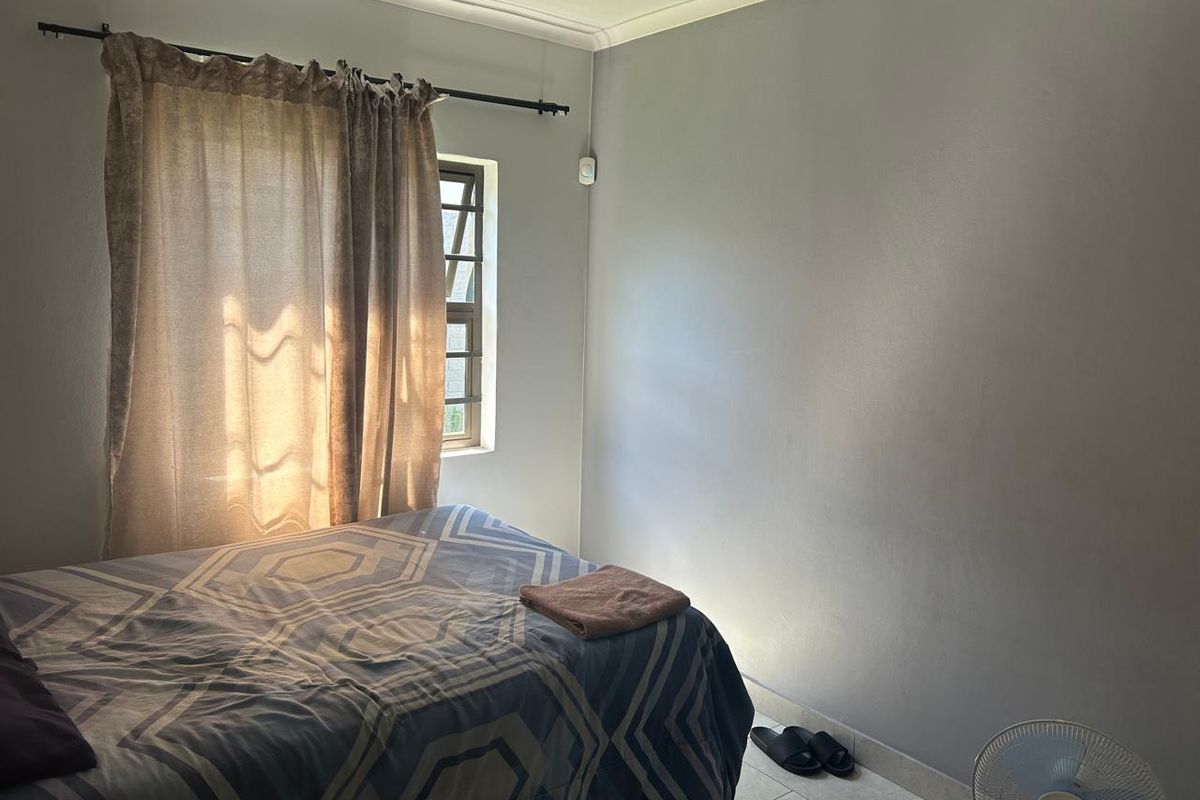 A functional bedroom featuring tiled flooring, neutral wall finishes, and a window fitted with security bars.