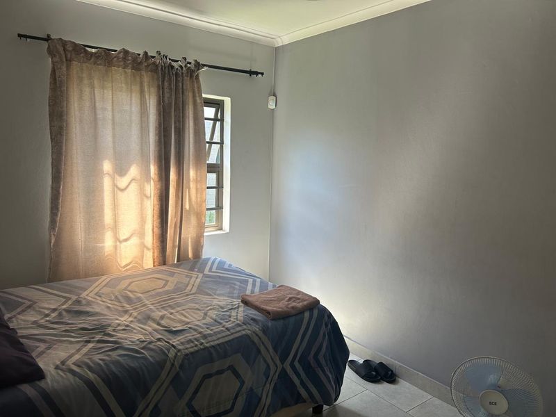 A functional bedroom featuring tiled flooring, neutral wall finishes, and a window fitted with security bars.