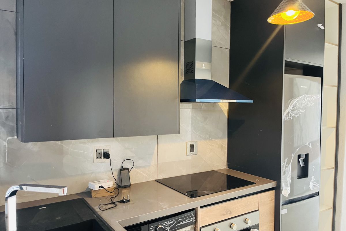 Modern kitchen featuring dark cabinetry, stone countertops, integrated oven, electric hob, extractor fan, and a sleek tiled backsplash.