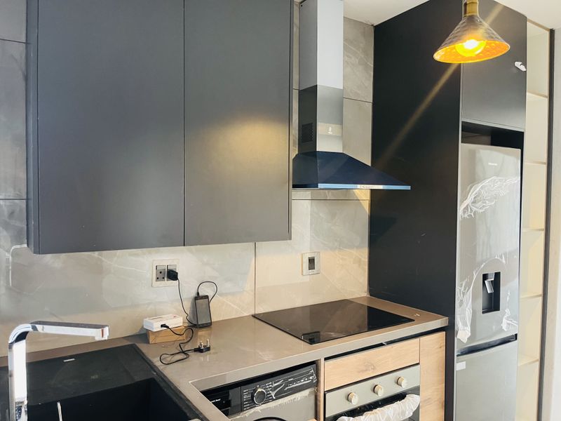Modern kitchen featuring dark cabinetry, stone countertops, integrated oven, electric hob, extractor fan, and a sleek tiled backsplash.