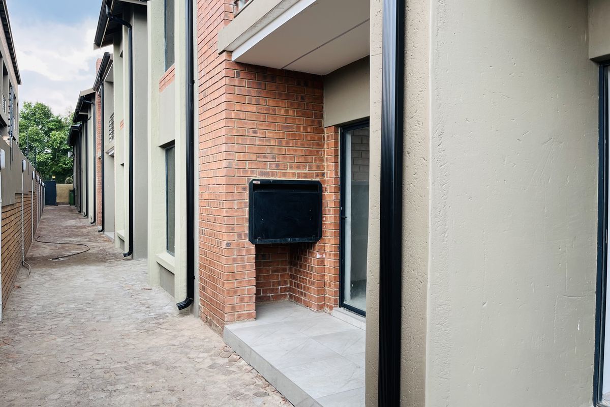 Rear exterior view of the apartment featuring a paved walkway, brick facade, and a built-in braai area on the patio.