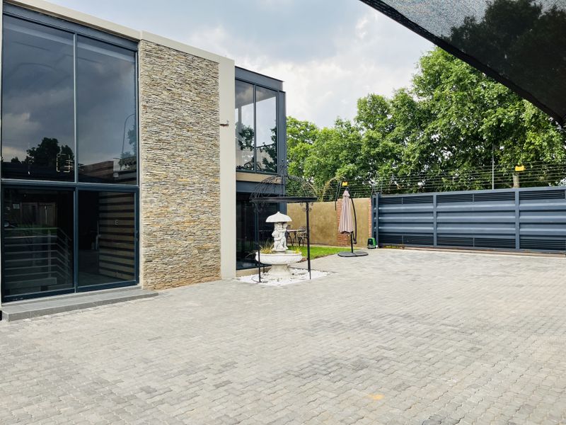 Modern apartment exterior featuring stone cladding, expansive glass sliding doors, and a spacious paved driveway with secure perimeter fencing.