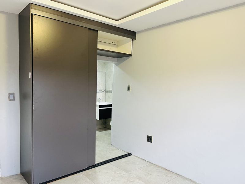 A bedroom featuring a large built-in sliding door wardrobe, recessed ceiling lighting, and tiled flooring, with an adjacent view into a bathroom.