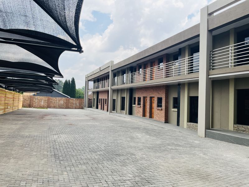 Exterior view of a modern apartment complex featuring a paved driveway, covered parking bays, and multi-level units with brick accents and balcony railings.