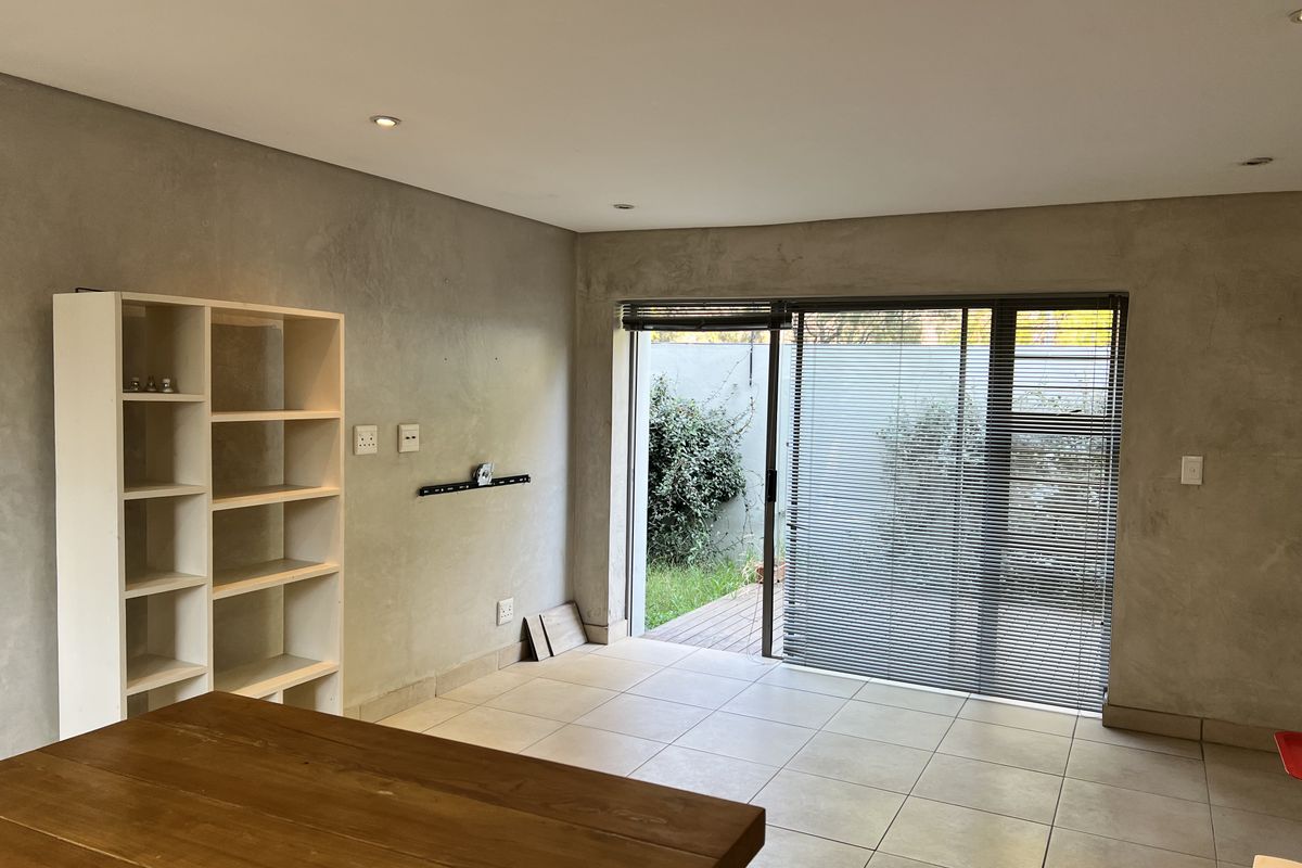 A bright, open-plan living area featuring modern cement-finish walls, tiled flooring, and large sliding glass doors that open onto a private outdoor space.