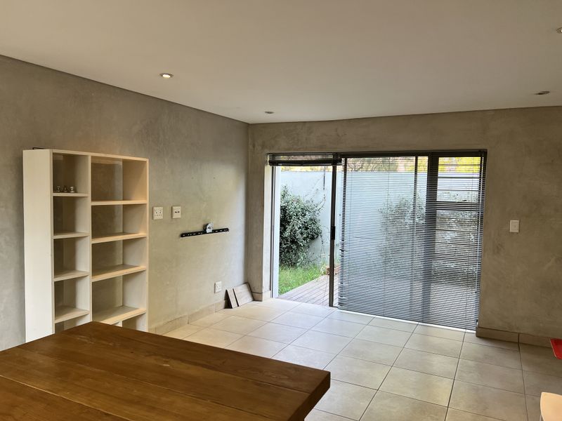 A bright, open-plan living area featuring modern cement-finish walls, tiled flooring, and large sliding glass doors that open onto a private outdoor space.