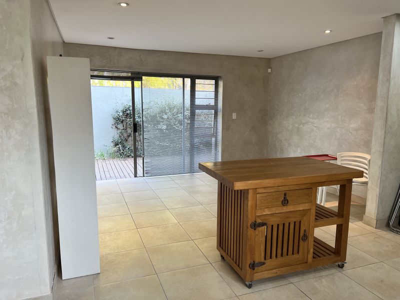 An open-plan living area featuring modern cementitious wall finishes, tiled flooring, recessed downlights, and a sliding glass door leading to an outdoor patio.
