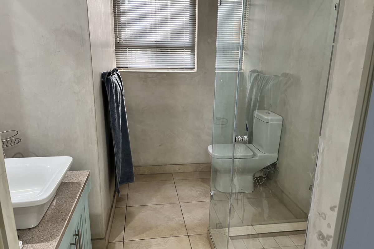 A functional bathroom featuring a vessel sink on a stone vanity, a glass-enclosed shower, and neutral tiled flooring.