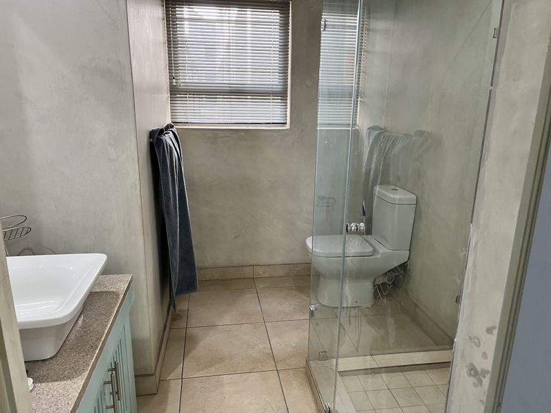 A functional bathroom featuring a vessel sink on a stone vanity, a glass-enclosed shower, and neutral tiled flooring.