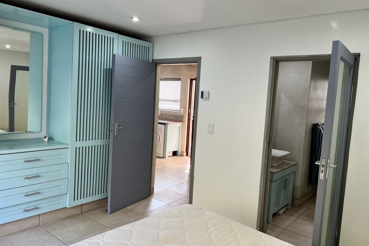 Bedroom featuring built-in light blue cabinetry with integrated vanity, tiled flooring, and direct access to an en-suite bathroom and adjacent utility area.