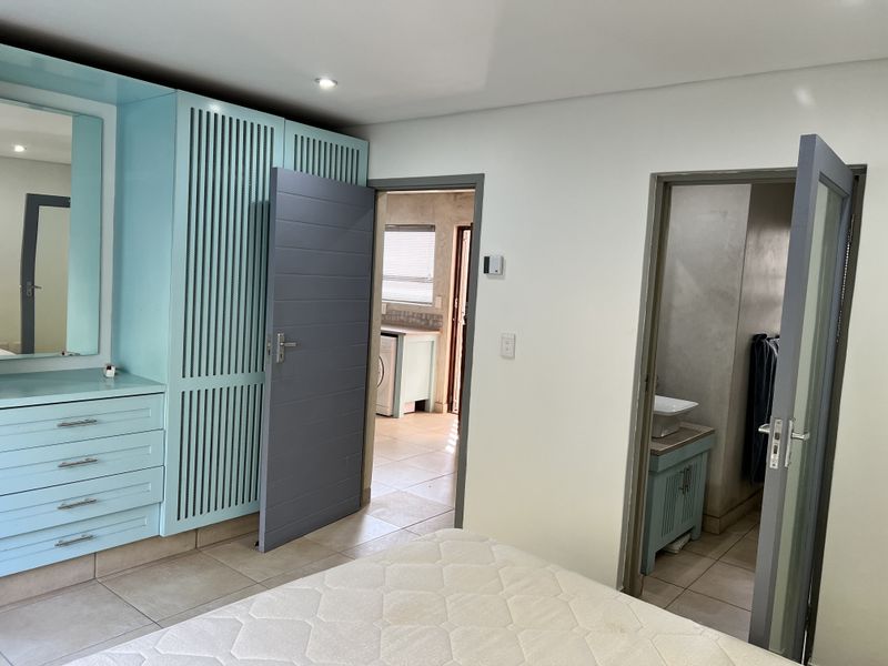 Bedroom featuring built-in light blue cabinetry with integrated vanity, tiled flooring, and direct access to an en-suite bathroom and adjacent utility area.