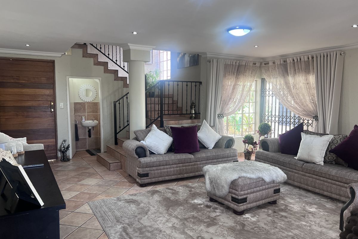 Spacious living area featuring tiled flooring, a wrought iron staircase, and an integrated guest cloakroom with a wall-mounted basin.