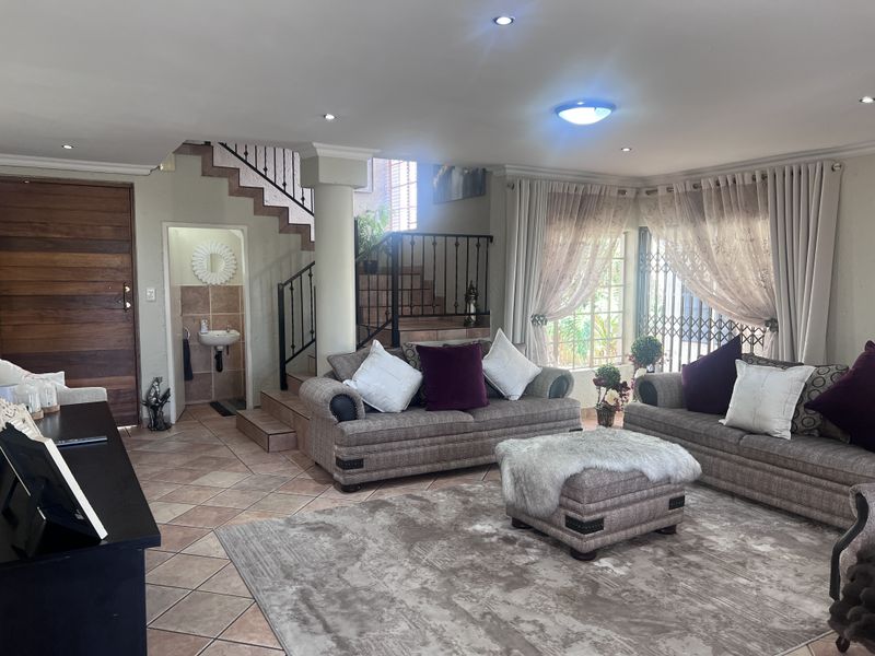 Spacious living area featuring tiled flooring, a wrought iron staircase, and an integrated guest cloakroom with a wall-mounted basin.