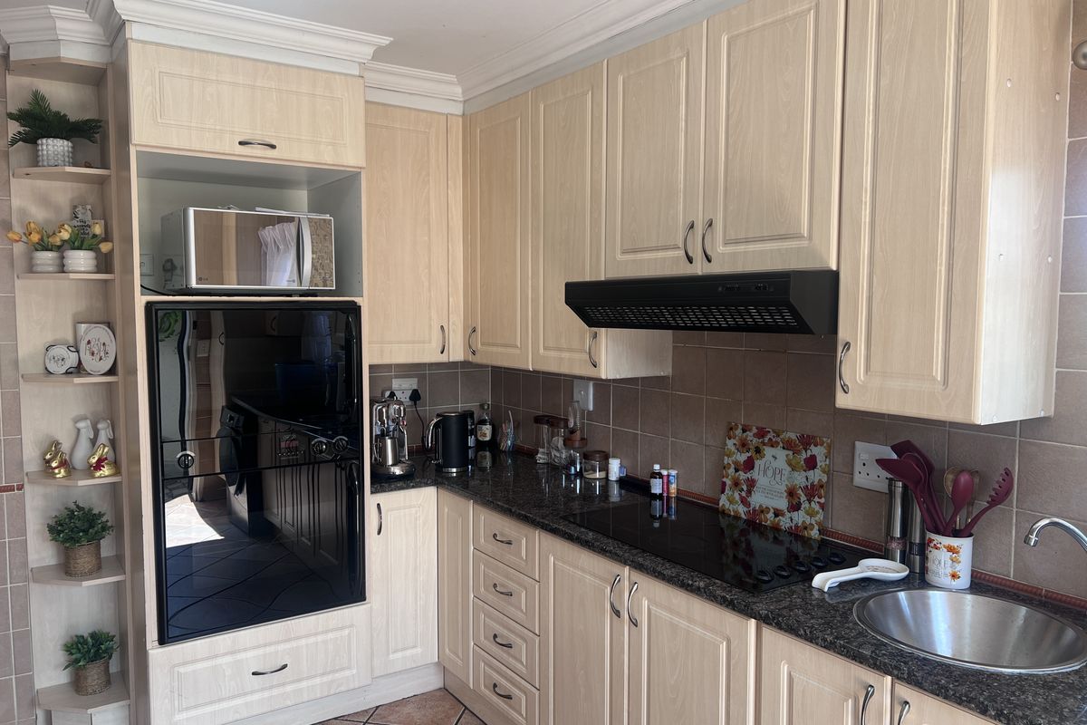 Functional kitchen featuring light wood cabinetry, granite countertops, built-in oven, electric hob, and tiled finishes throughout.