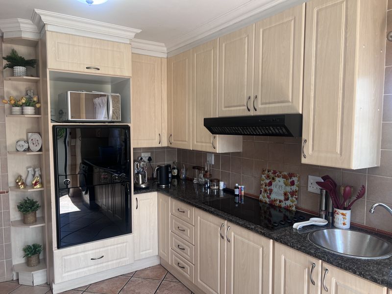 Functional kitchen featuring light wood cabinetry, granite countertops, built-in oven, electric hob, and tiled finishes throughout.