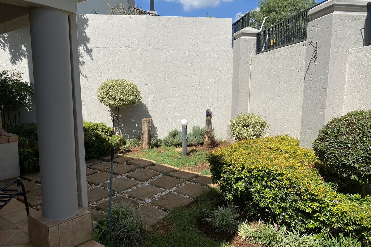 A private rear garden area featuring a paved patio, established landscaping, and high boundary walls for added privacy.