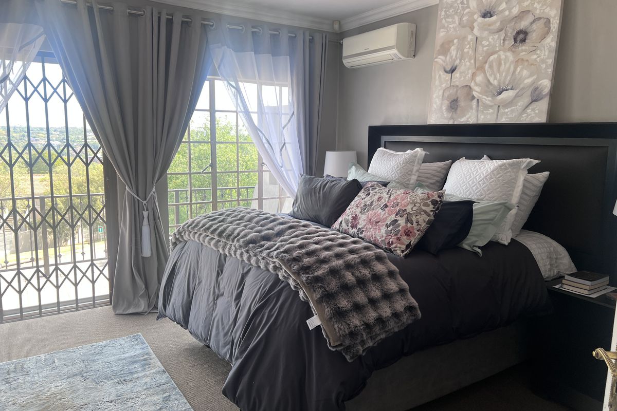 A well-maintained bedroom featuring crown molding, a wall-mounted air conditioning unit, and a sliding door leading to a balcony with a security gate.