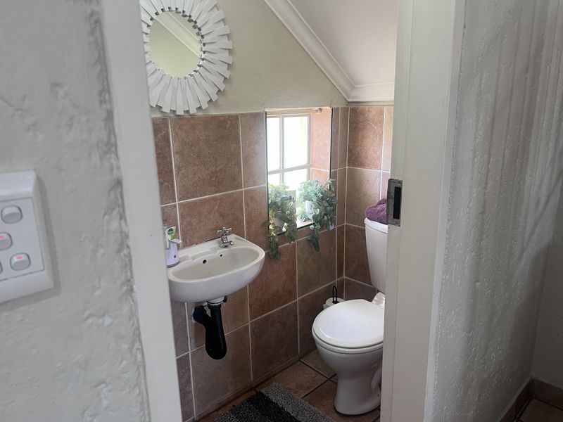 A compact guest bathroom featuring tiled walls, a wall-mounted basin, and a toilet, situated under a sloped ceiling.