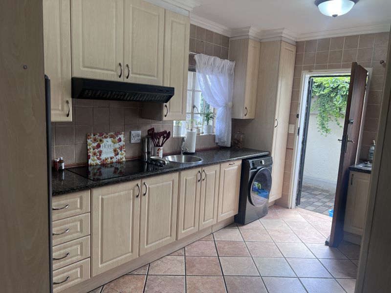 A functional kitchen featuring light wood cabinetry, granite countertops, a built-in hob with extractor, and direct access to an outdoor area.