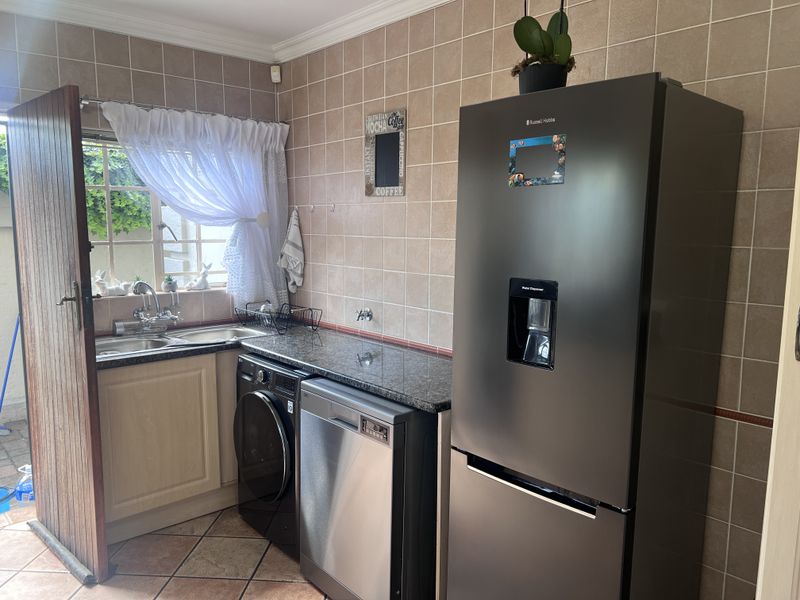 A functional laundry area featuring a double basin sink, granite countertops, tiled backsplash, and tiled flooring with direct access to the exterior.
