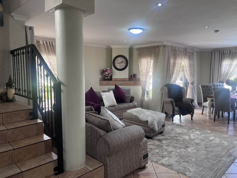 Spacious open-plan living and dining area featuring tiled flooring, a built-in fireplace, and a decorative wrought iron staircase railing.