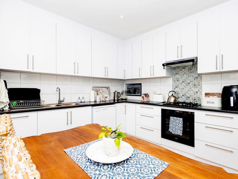 A modern, well-maintained kitchen featuring white cabinetry, black granite countertops, a built-in oven, gas hob, and a decorative tiled backsplash.
