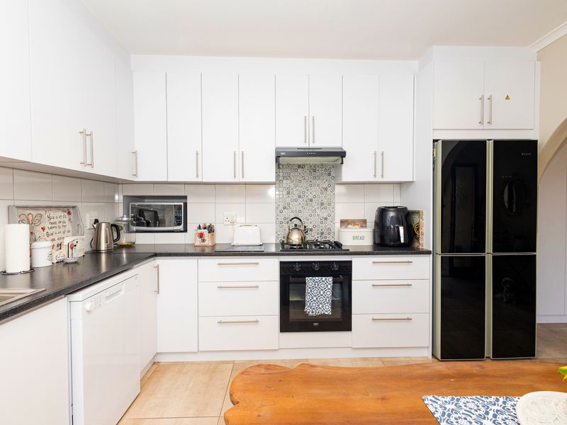 A well-maintained kitchen featuring white cabinetry, dark countertops, a gas hob with extractor, and integrated appliances, offering a clean and functional cooking space.