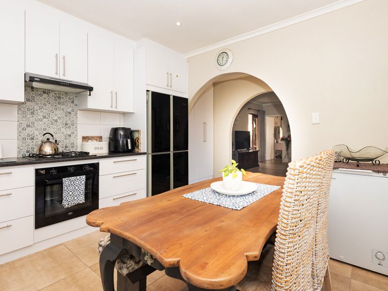 Modern kitchen featuring white cabinetry, stone countertops, gas hob, electric oven, and a decorative tiled splashback, leading through an archway to the living area.