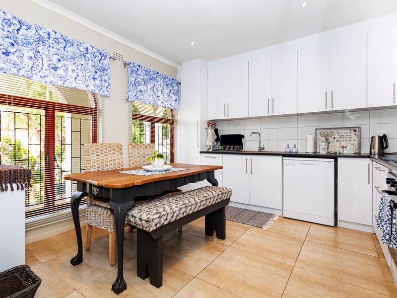 A functional kitchen featuring white cabinetry, tiled flooring, a built-in oven, and a dining area with large windows and security bars.