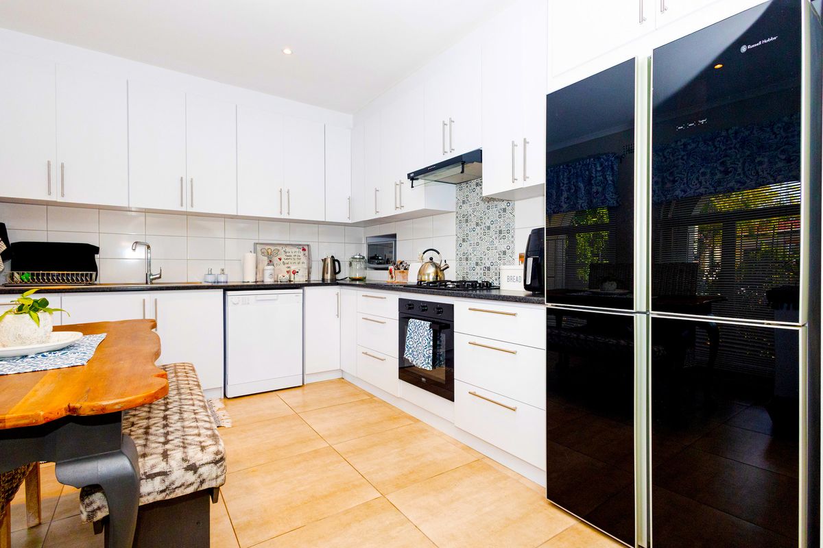 Modern kitchen featuring white cabinetry, dark stone countertops, tiled backsplash, built-in oven, gas cooktop, and integrated dishwasher.
