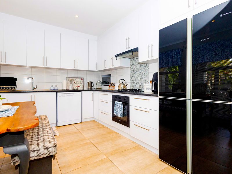 Modern kitchen featuring white cabinetry, dark stone countertops, tiled backsplash, built-in oven, gas cooktop, and integrated dishwasher.