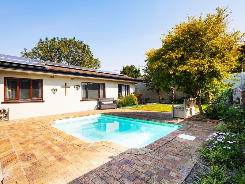 A well-maintained backyard featuring a swimming pool, brick-paved patio area, and established garden surroundings.