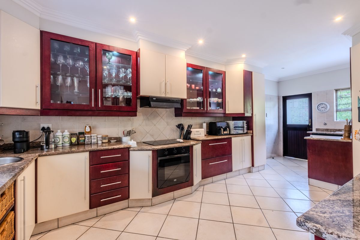 Spacious kitchen featuring two-tone cabinetry, granite countertops, built-in oven with hob, extractor fan, and tiled flooring, leading to an exterior door.