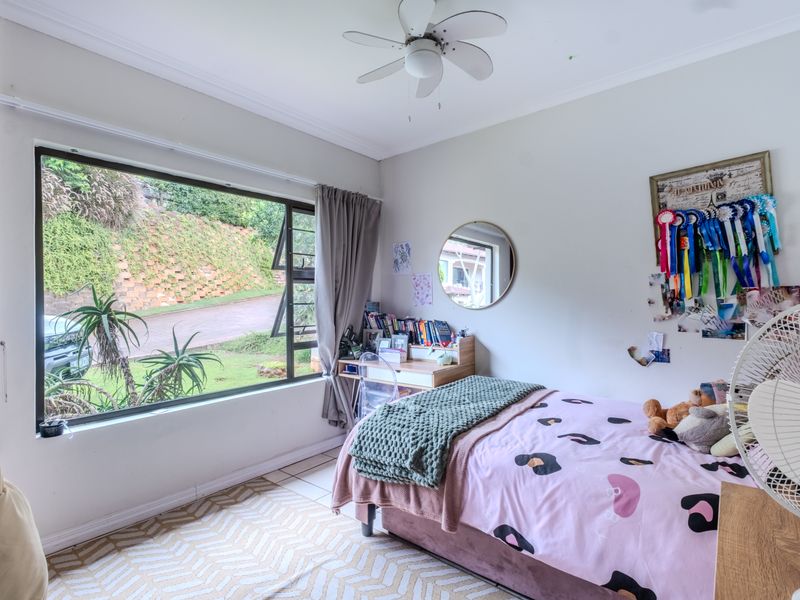 A well-lit bedroom featuring tiled flooring, a ceiling fan, and a large window providing natural light and views of the exterior.