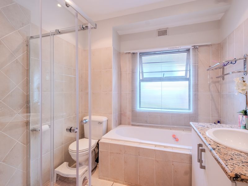 A functional bathroom featuring a glass-enclosed shower, a built-in bathtub, and a granite-topped vanity with an undermount sink.