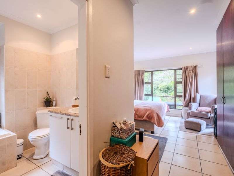 Spacious bedroom featuring tiled flooring, built-in cupboards, and an integrated en-suite bathroom with a vanity and bathtub, overlooking a lush garden view.