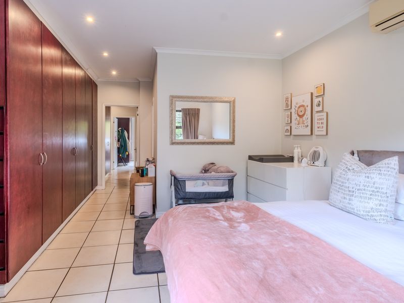 A well-maintained bedroom featuring extensive floor-to-ceiling built-in cupboards, tiled flooring, and a wall-mounted air conditioning unit, leading into a hallway.