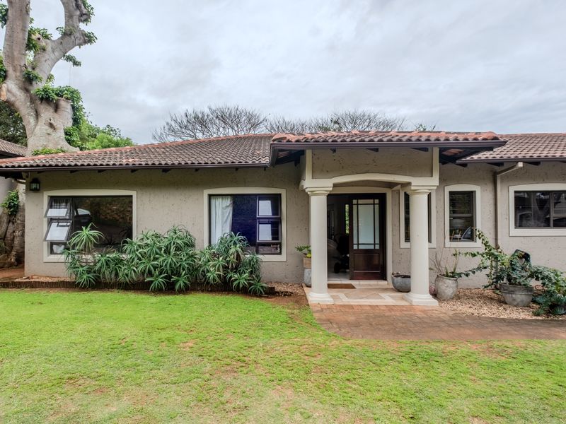 Front elevation of a townhouse featuring a tiled roof, covered entrance with concrete columns, and established garden area.